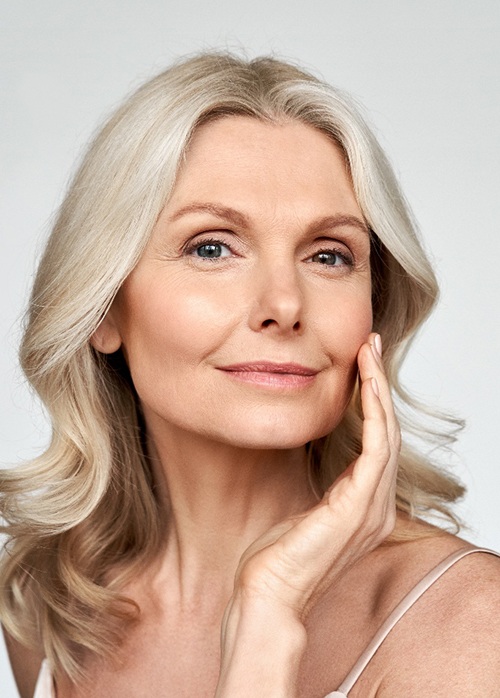Woman with long blond hair touching her hand to her smooth cheek