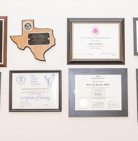 Several framed diplomas and plaques on wall of dental office