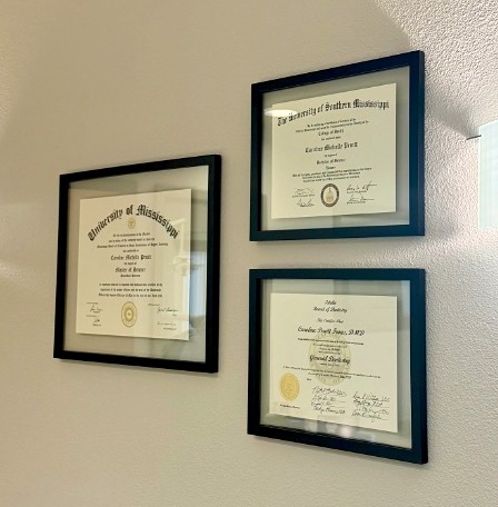 Several framed diplomas and plaques on wall of dental office