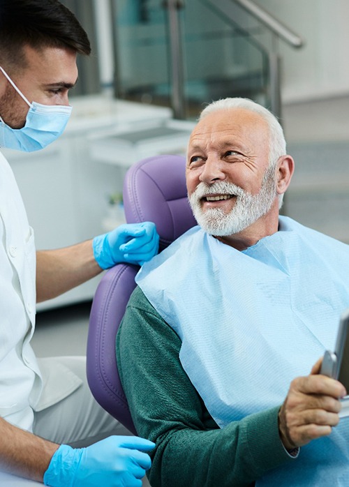 Senior patient looking at dentist while holding small mirror