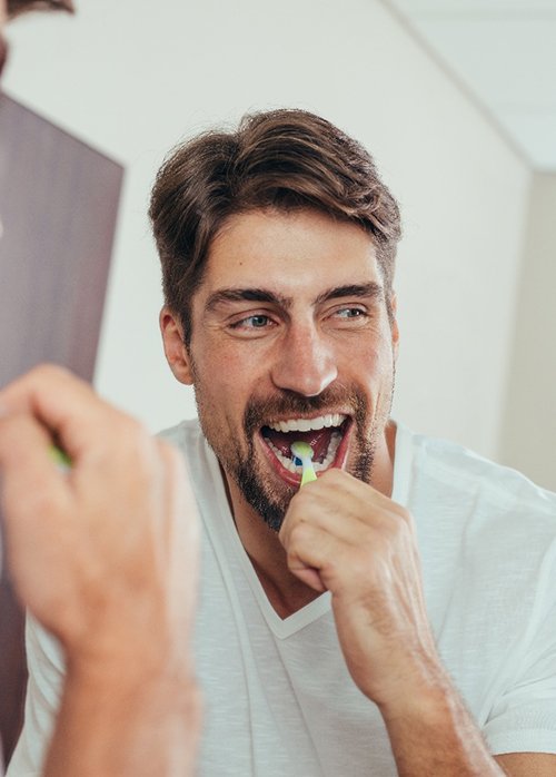 Man smiling while brushing his teeth